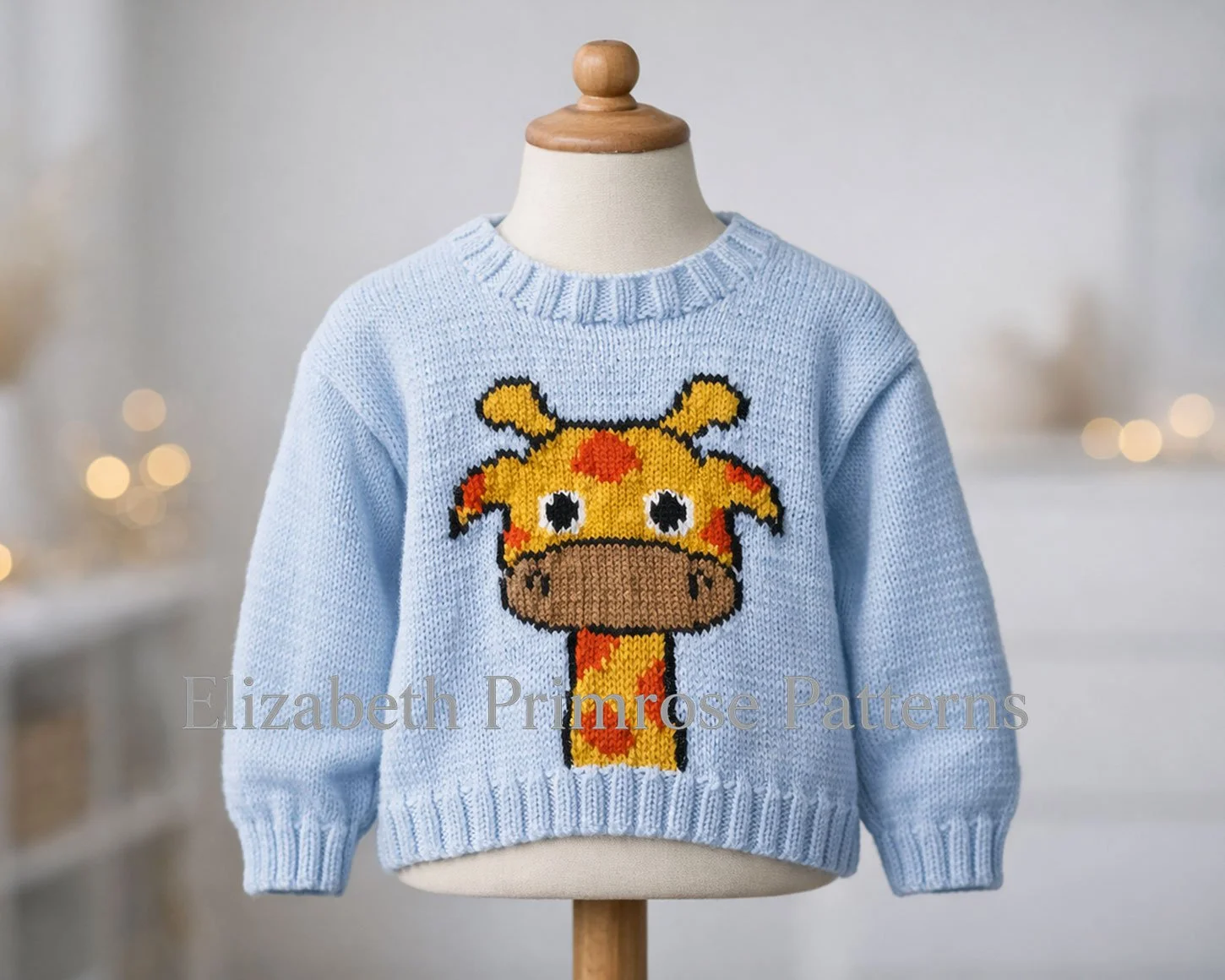Children’s blue knitted jumper with giraffe motif displayed on a fabric mannequin against a blurred, cosy background with gentle warm lighting.
