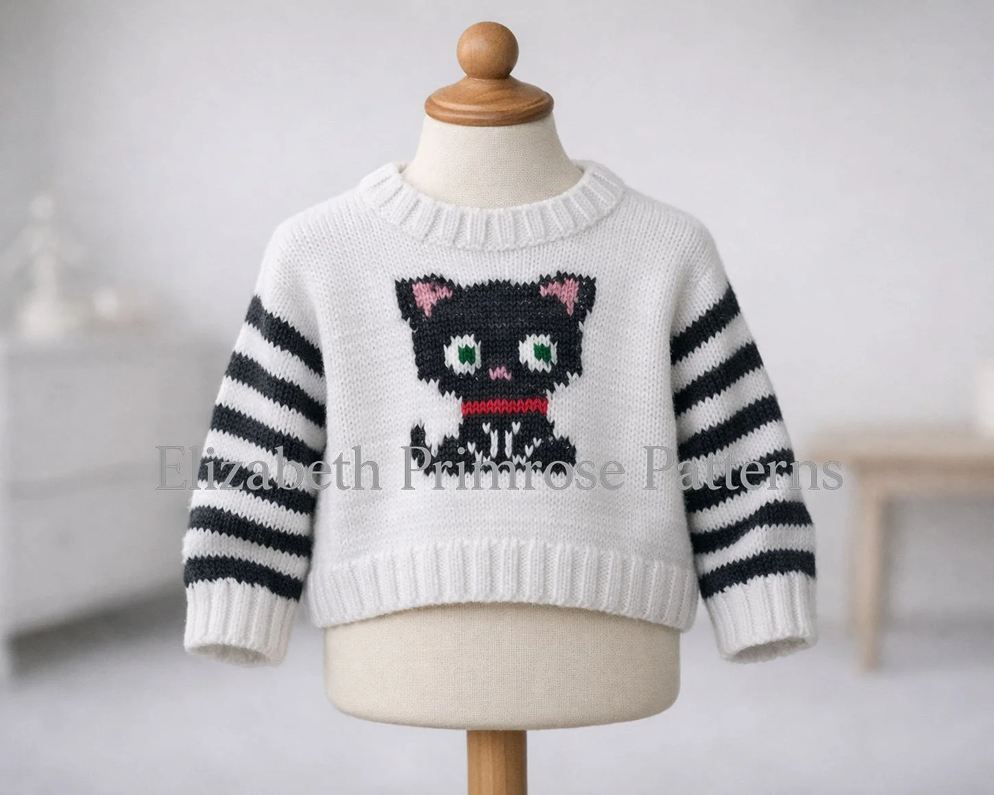 White jumper with grey striped sleeves and a knitted cat motif displayed on a child’s mannequin in a clean, softly lit Scandinavian style room.