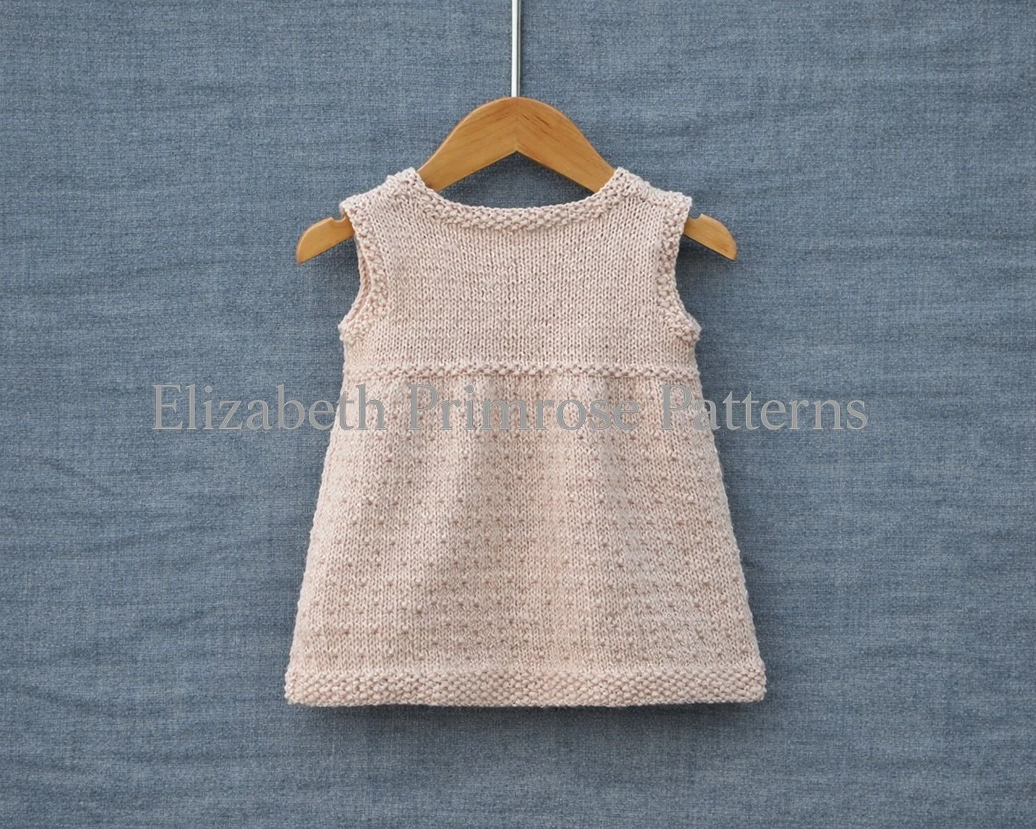 Back view of sleeveless cream dress with dotty skirt pattern and moss stitch edgings on a hanger and blue background.