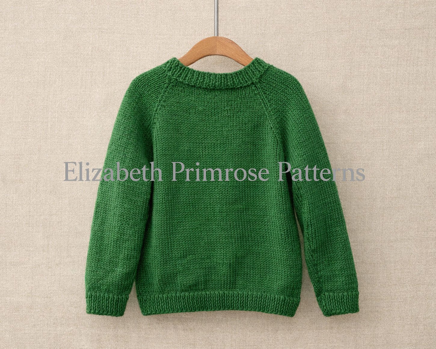 Green knitted children’s back view of jumper hanging on a wooden hanger against a beige fabric background, showing ribbed neckline, cuffs, and hem.