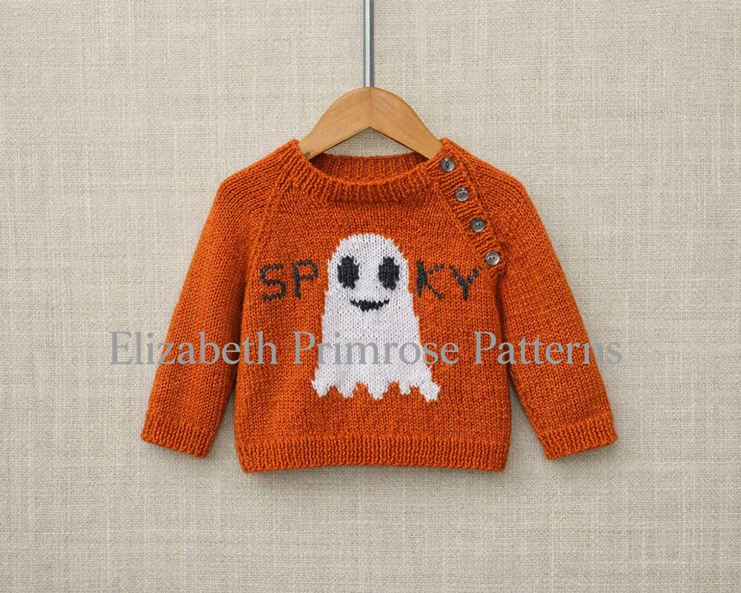 Halloween‑themed orange jumper featuring ghost motif and “spooky” text, displayed on hanger with neat ribbing and buttoned shoulder in a soft neutral setting.