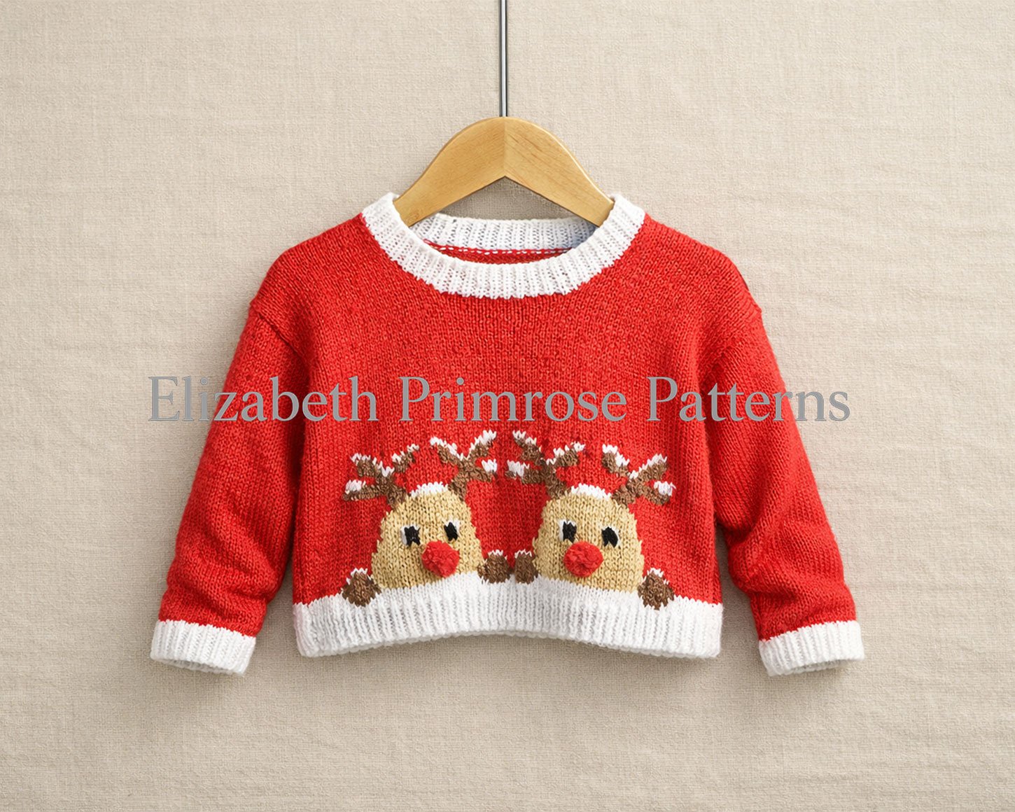 Red children’s jumper on a wooden hanger with two red nosed reindeers peeking from the snowy hem against a soft beige background.
