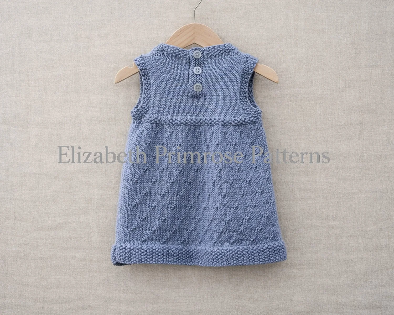 Back view of a grey sleeveless knitted dress on a hanger, featuring moss stitch edgings, a three-button band, and a textured skirt