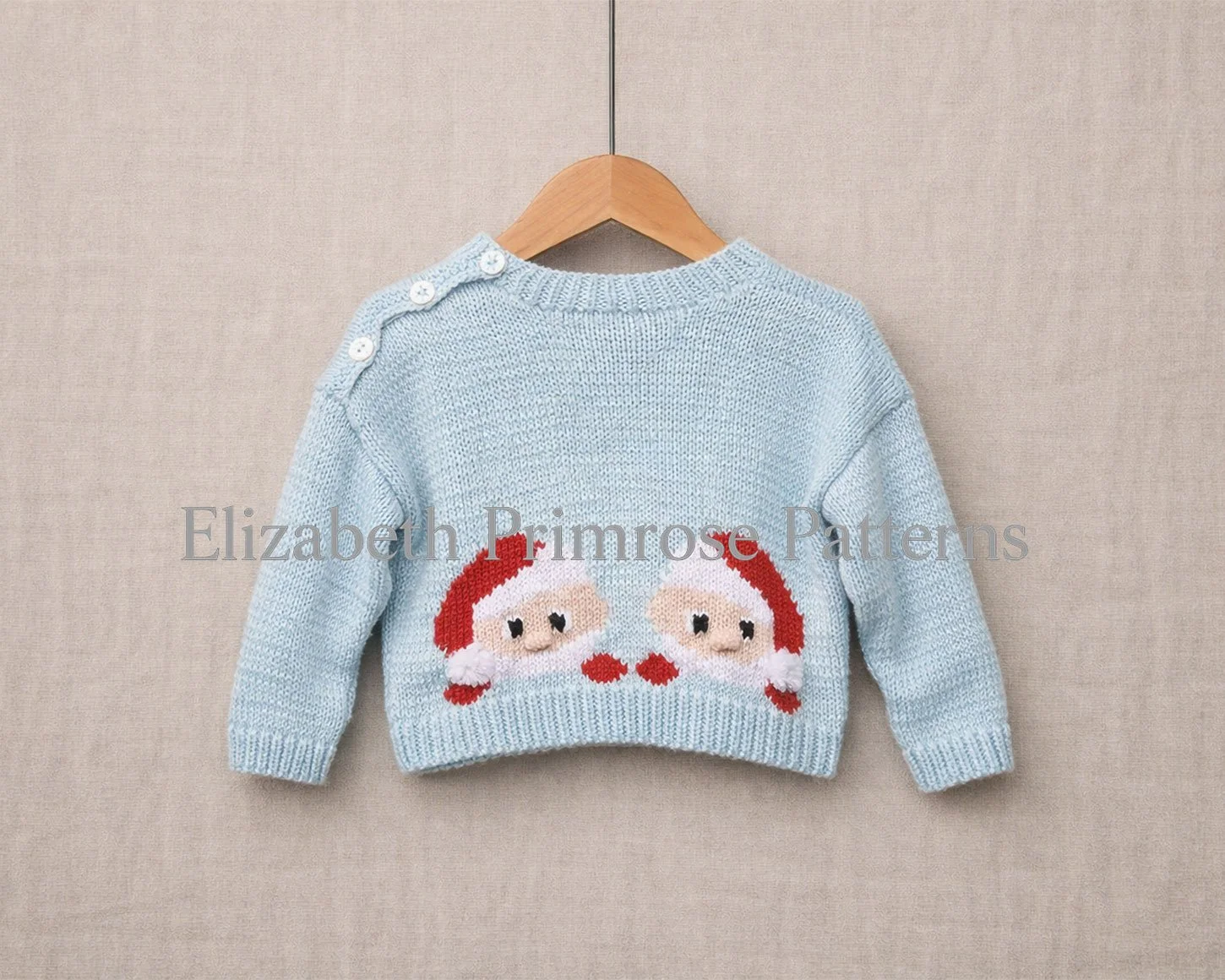 Back of a light blue children’s jumper on a wooden hanger, showing peeking Santa motif with shoulder buttons against a soft beige background.