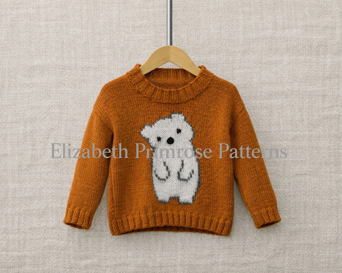 Rust orange children’s jumper with a white bear motif hanging on a wooden hanger against a soft beige background.