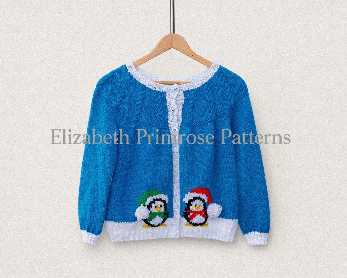 Soft blue knitted cardigan with white edging and two penguin designs, hanging neatly on a wooden hanger against a simple, uncluttered backdrop.