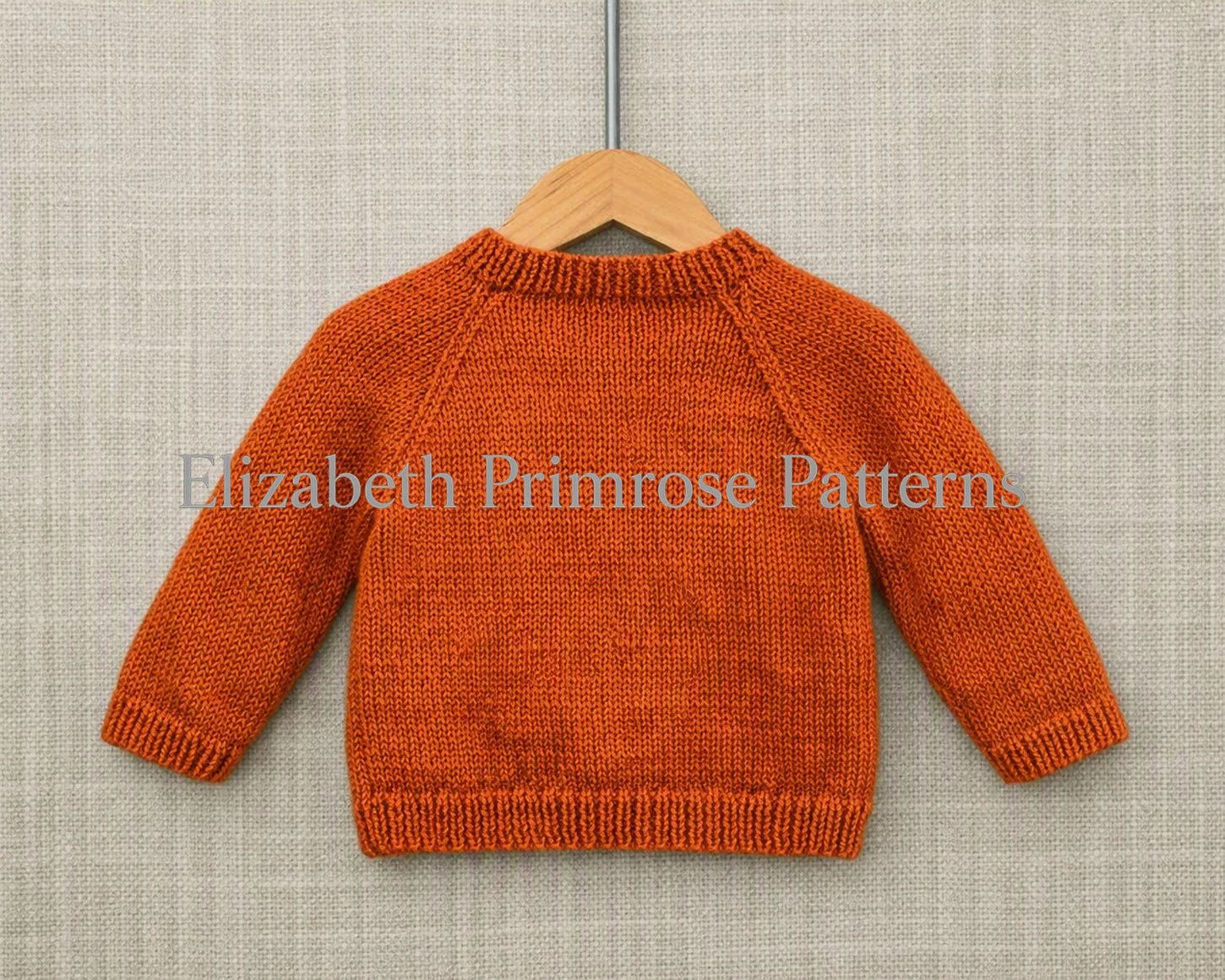 Back view of orange children’s jumper on hanger, showing neat raglan shaping, ribbed edges and smooth stocking stitch fabric against a neutral textured background.