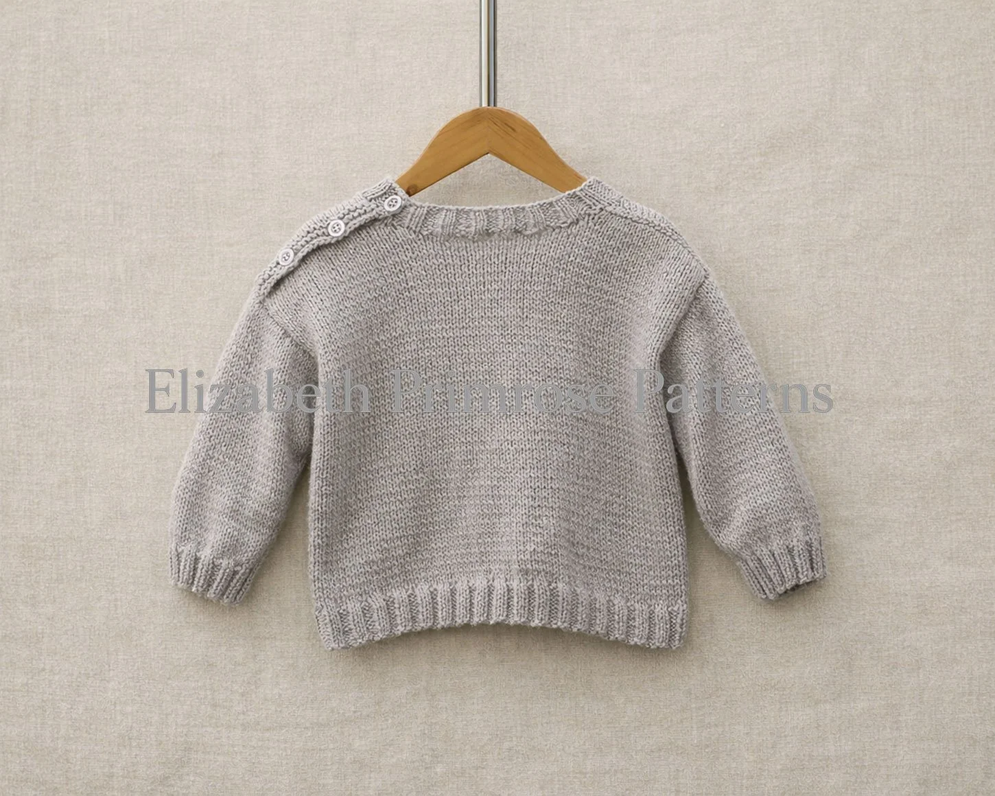 Grey children’s knitted jumper shown from the back, hanging on a wooden hanger against a textured beige fabric background.