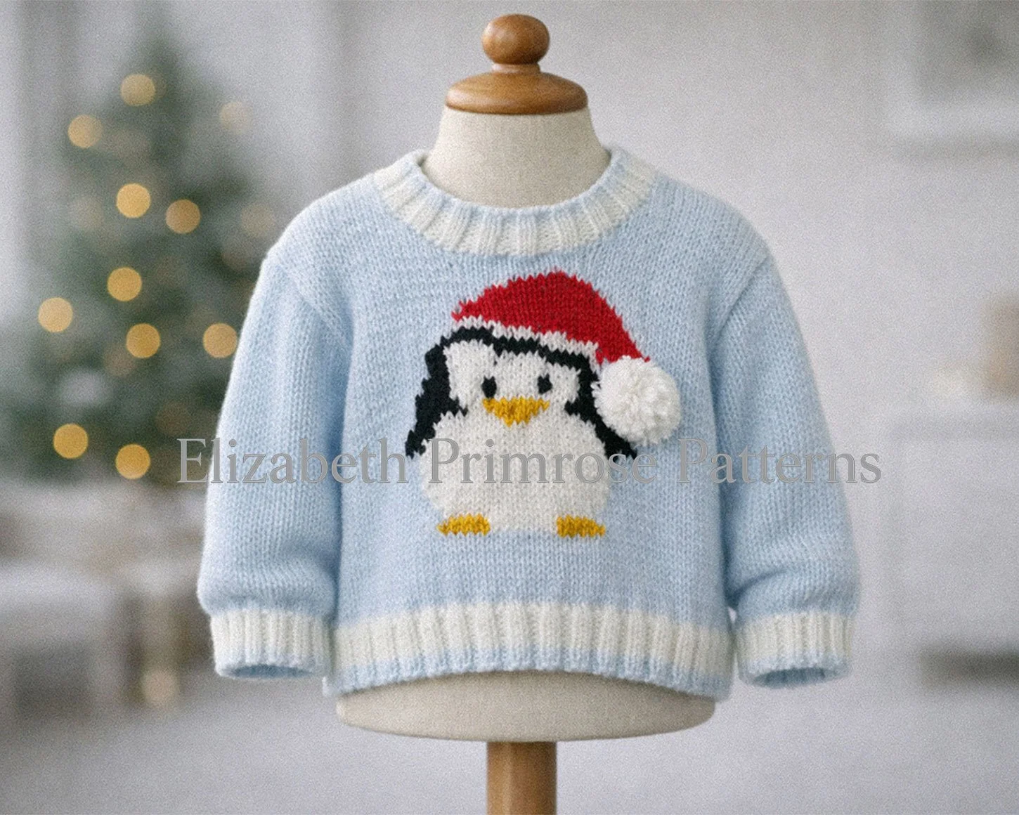 Knitted blue jumper with penguin motif and Santa hat displayed on a mannequin, shown in a softly lit Christmas room with warm blurred lights.
