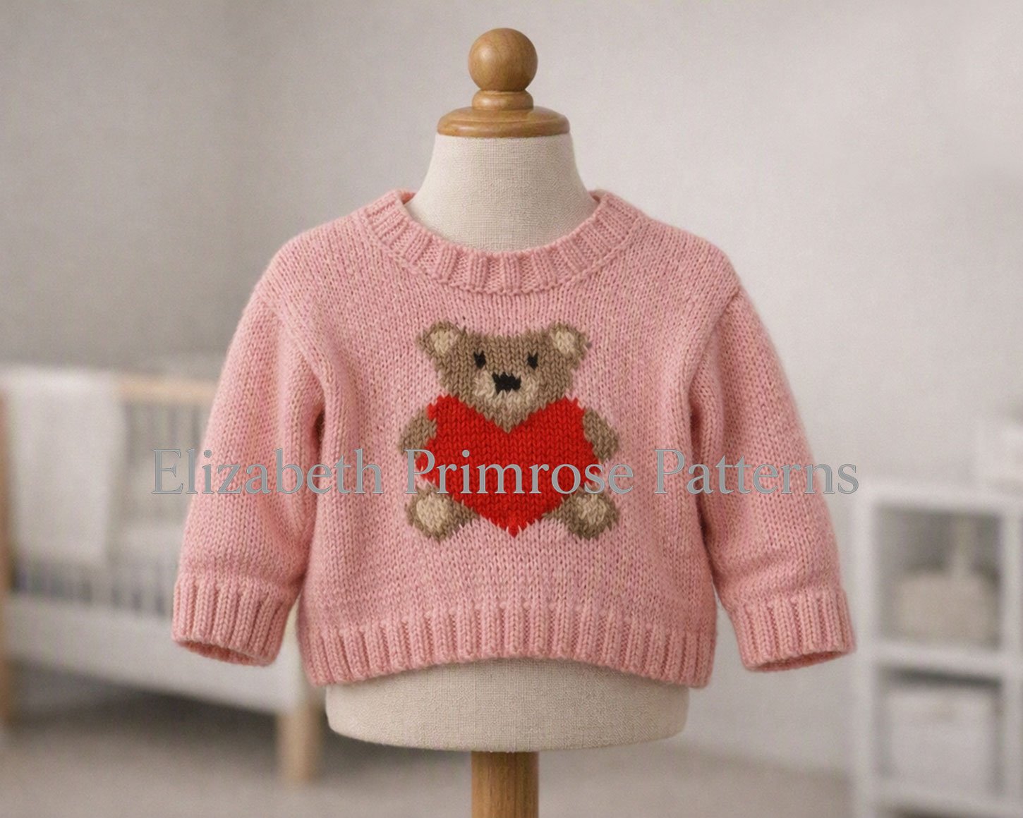 Soft pink knitted kids' sweater featuring an intarsia teddy bear holding a vibrant red heart, shown on a cream display mannequin.