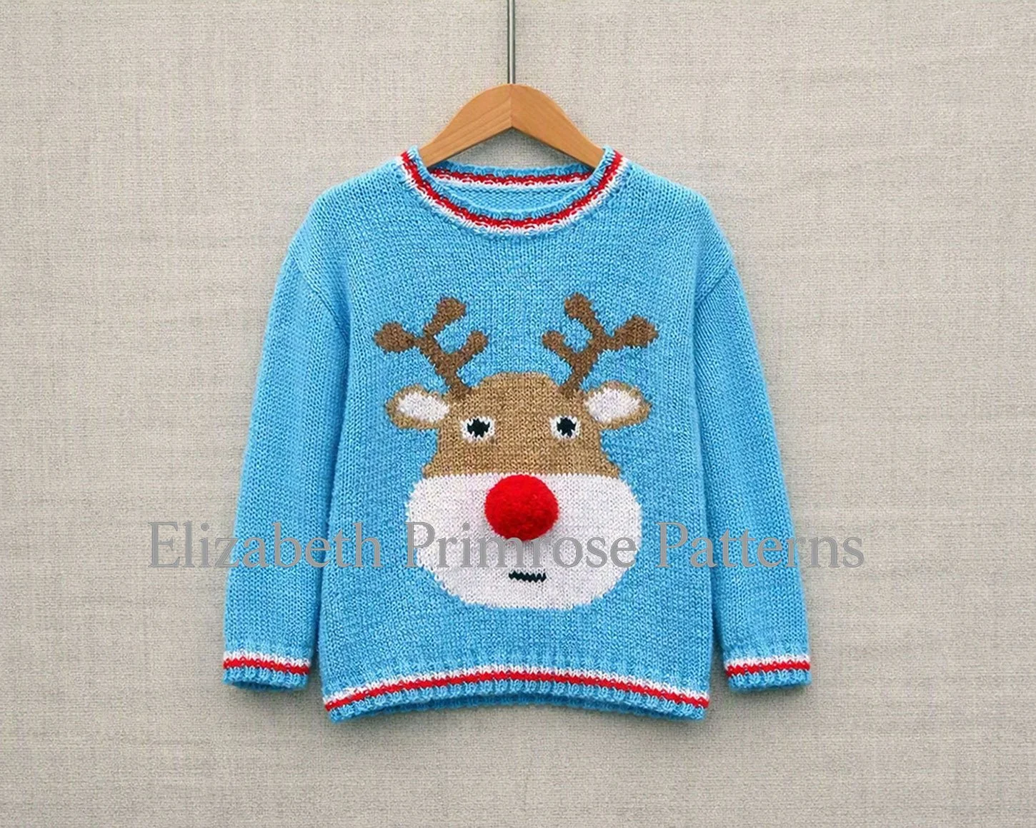 Light blue Christmas jumper with reindeer design, red white trim, hanging neatly against textured neutral fabric background.