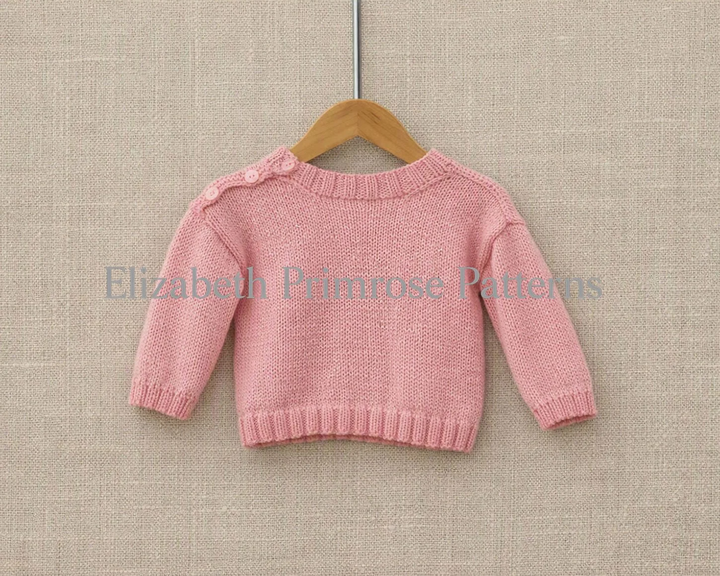 The back view of a hand-knitted light pink children's sweater on a wooden hanger. The design features a plain stocking stitch back and three small buttons closing the left shoulder seam.