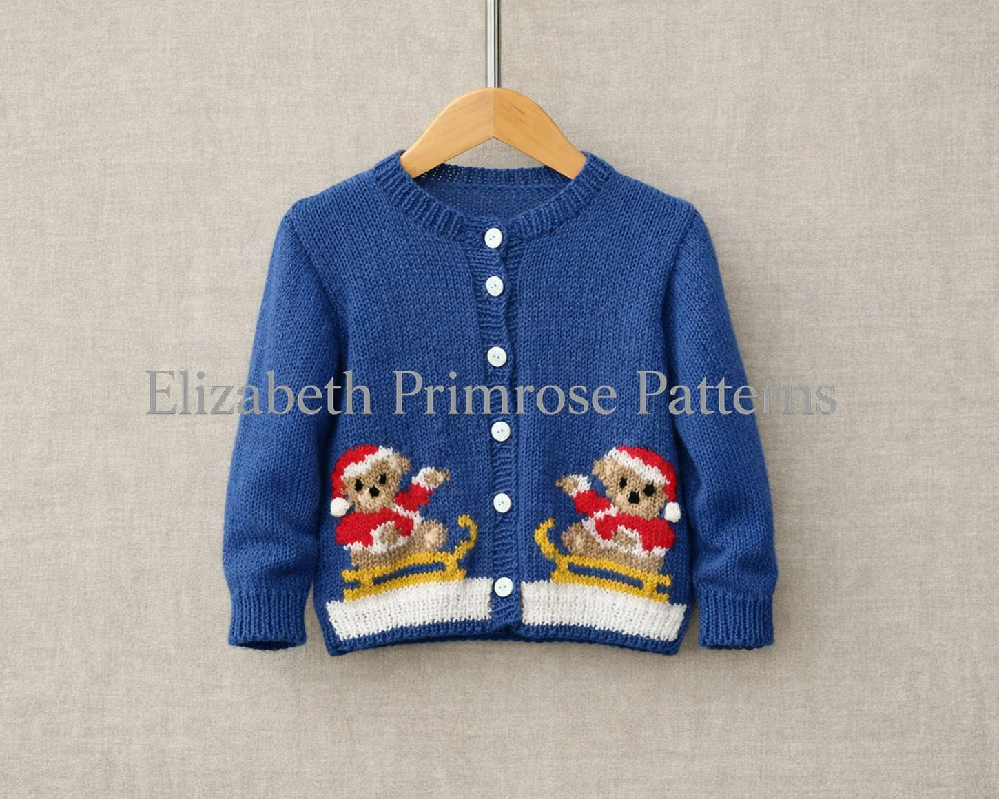 Blue children’s round neck cardigan with Christmas teddy bears on sleighs, displayed on a wooden hanger against a beige linen background.