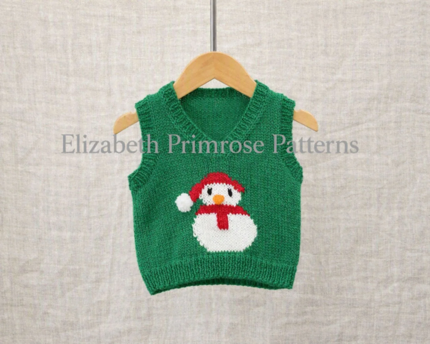 Children’s green snowman tank top with V neck on a wooden hanger against a linen backdrop.