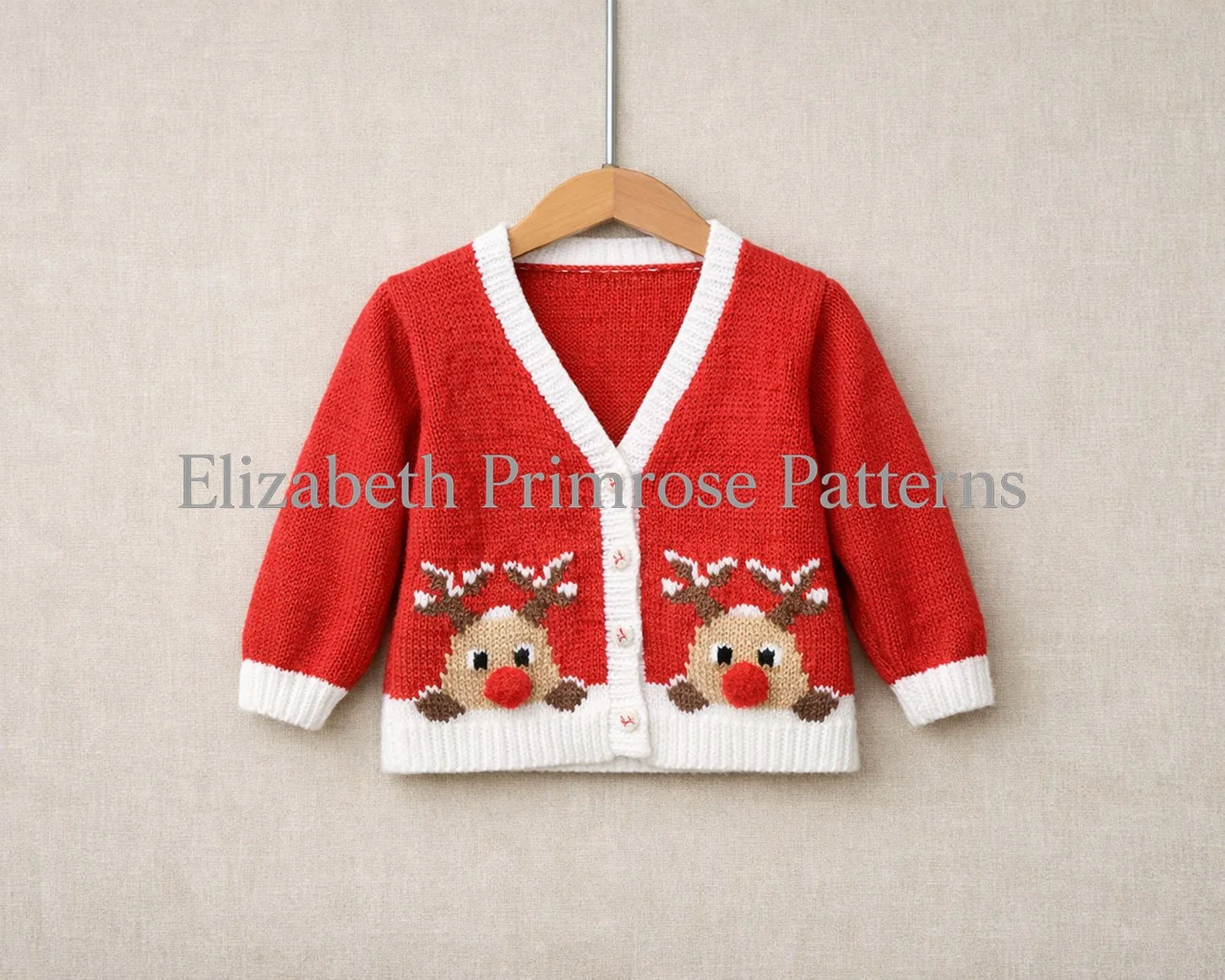 Red children’s v-neck cardigan on a wooden hanger with white trims and two Rudolph motifs, shown against a beige fabric background.