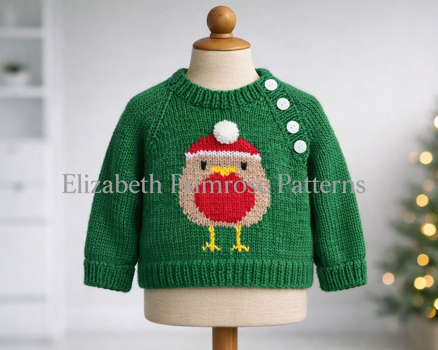 Green children’s jumper on mannequin featuring a festive robin motif and side buttons, with a softly lit Christmas tree in the background.