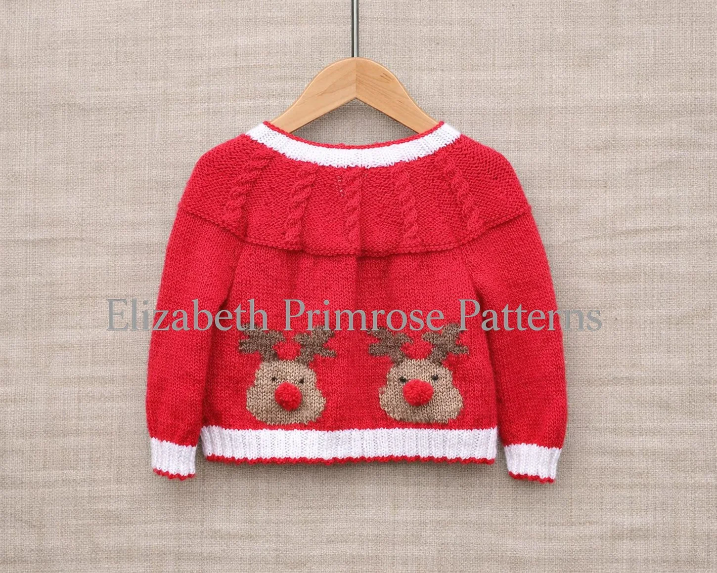 Red children’s Christmas jacket with reindeer motifs shown from the back on a wooden hanger against a beige linen background.
