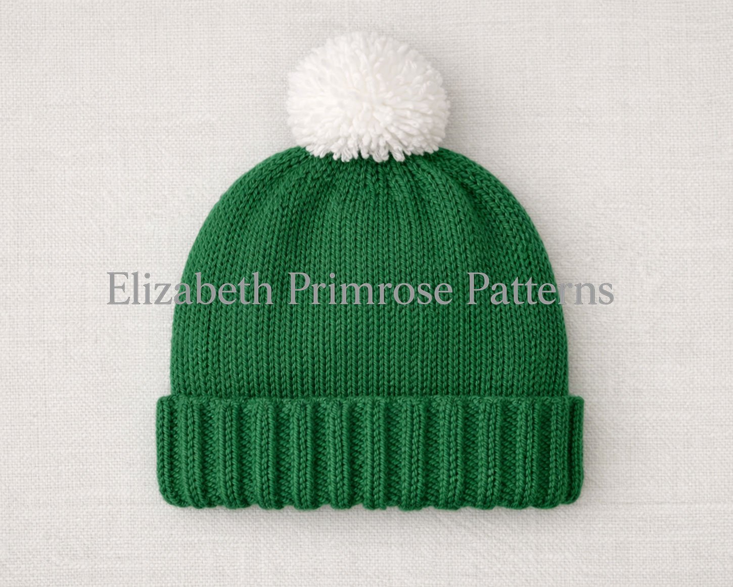 Back view of knitted green Christmas with white pompom, laid flat against a neutral fabric backdrop.
