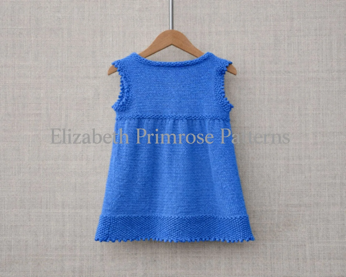 Back view of blue children’s dress shown on a wooden hanger with a crisp linen background.