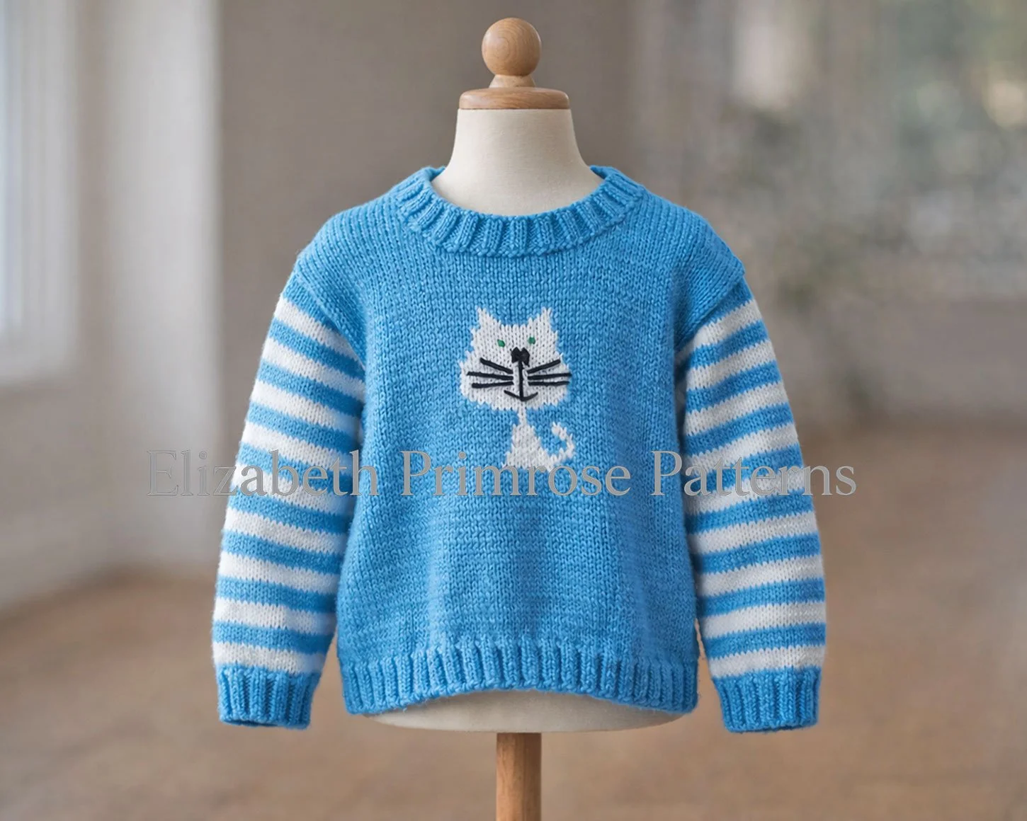 Hand knitted blue sweater featuring a white cat design and striped sleeves shown on a mannequin in a warm, blurred room setting.