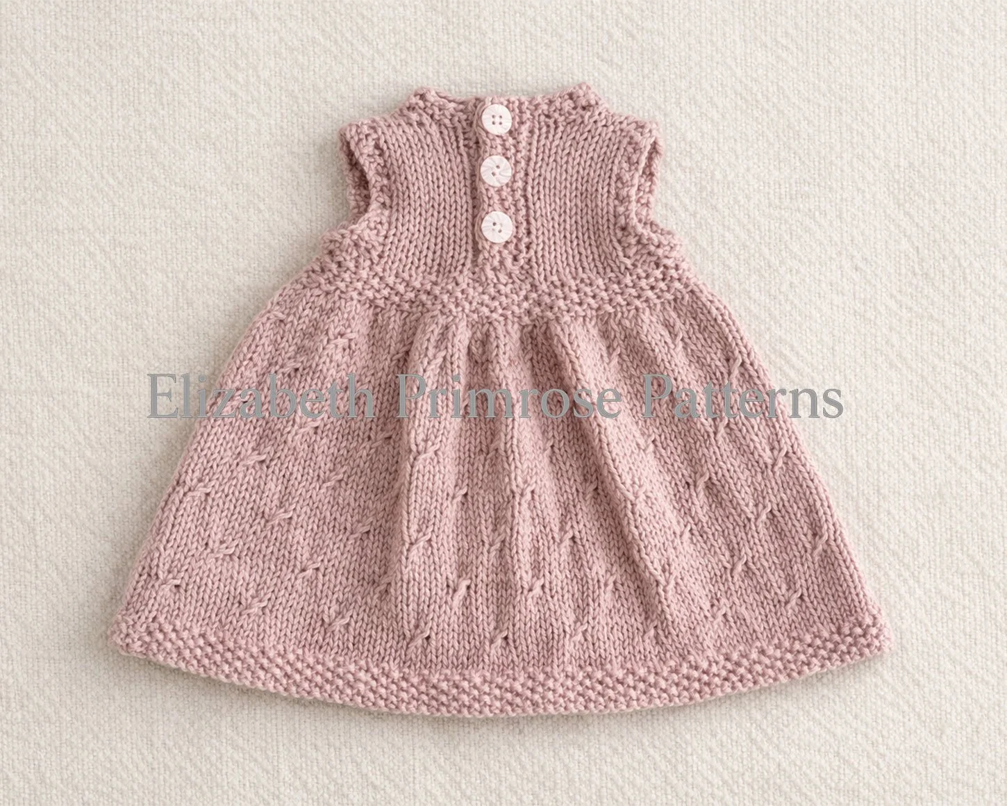 Back view of sleeveless pink knitted doll dress displayed on a neutral backdrop, showing diamond patterned skirt and moss stitch borders.
