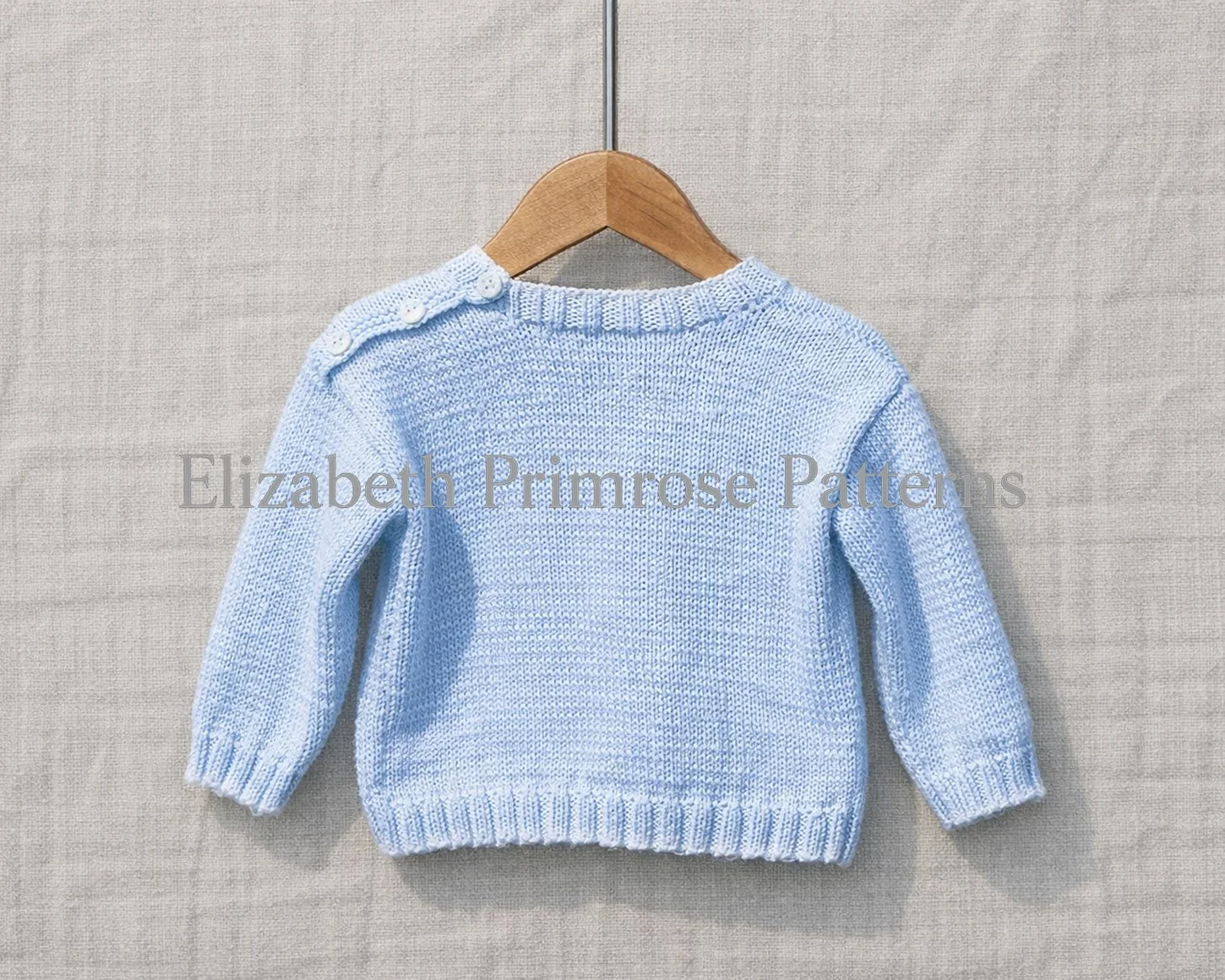 Back view of blue knitted toddler’s sweater displayed on a wooden hanger, shown against a calm, blurred textile backdrop.