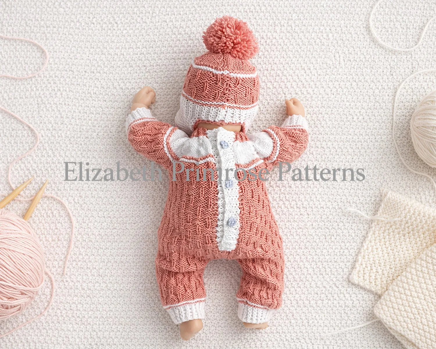 Back view of doll in pink and white knitted outfit with pom pom hat, lying on textured cream knitted surface surrounded by yarn balls, needles, and swatches.