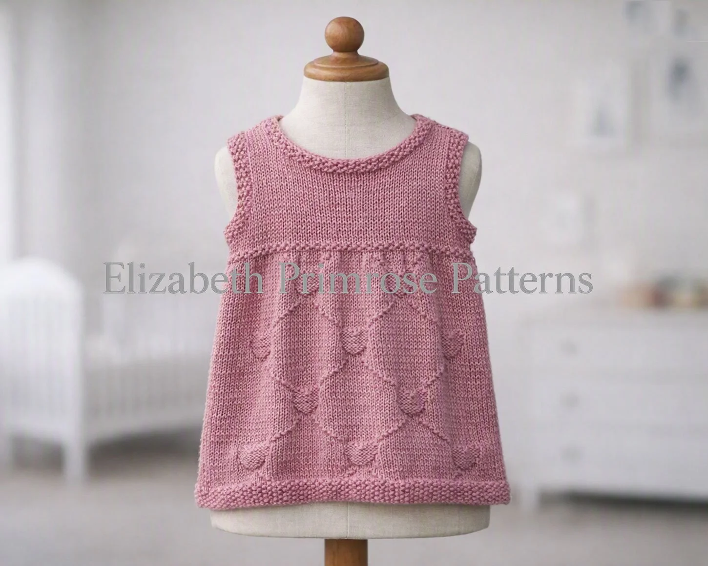 Dusty pink sleeveless hand-knitted child dress with textured diamond hearts pattern on a display mannequin.