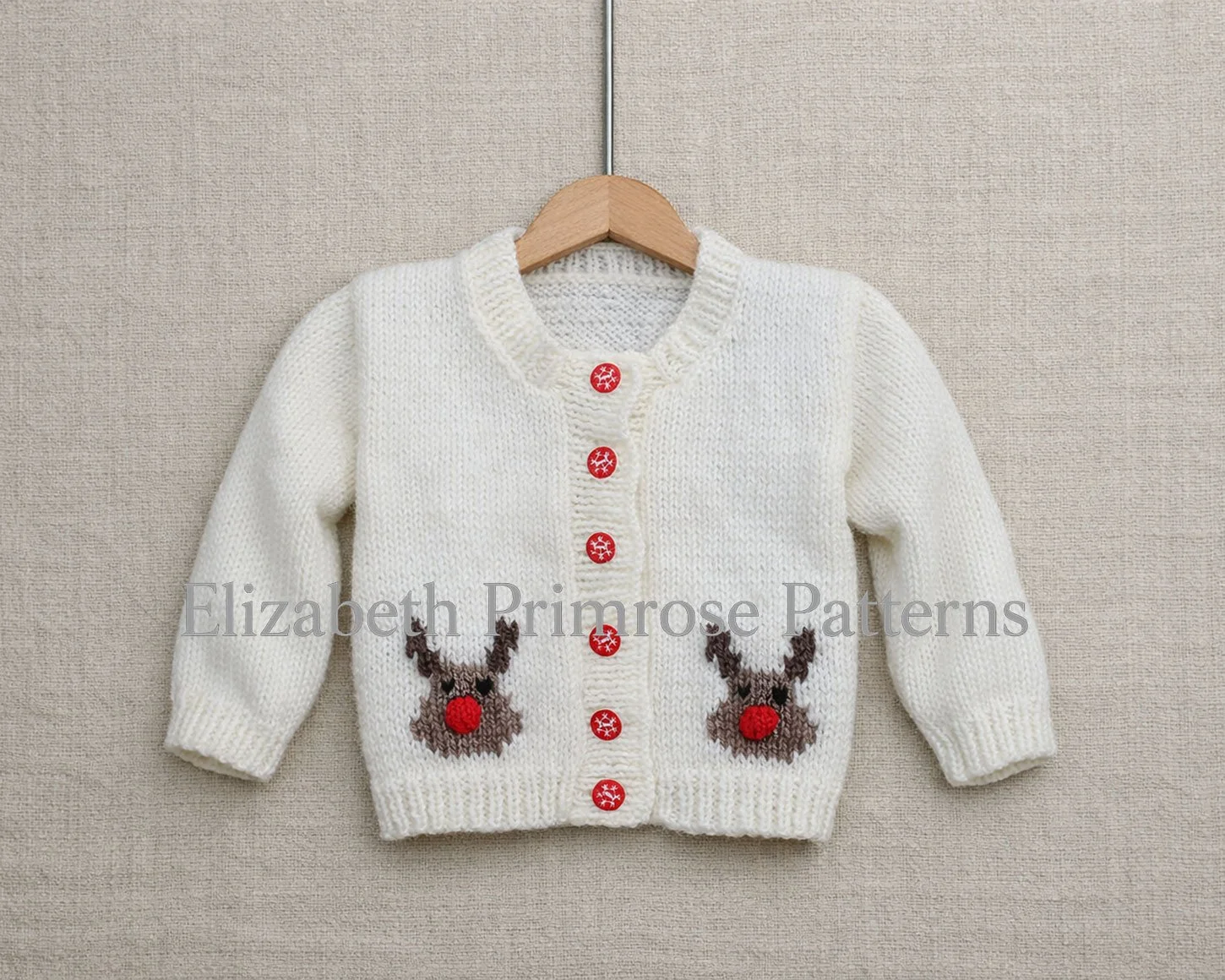 Cream baby cardigan with two Rudolph motifs and red snowflake buttons, displayed on a wooden hanger against a beige linen background.