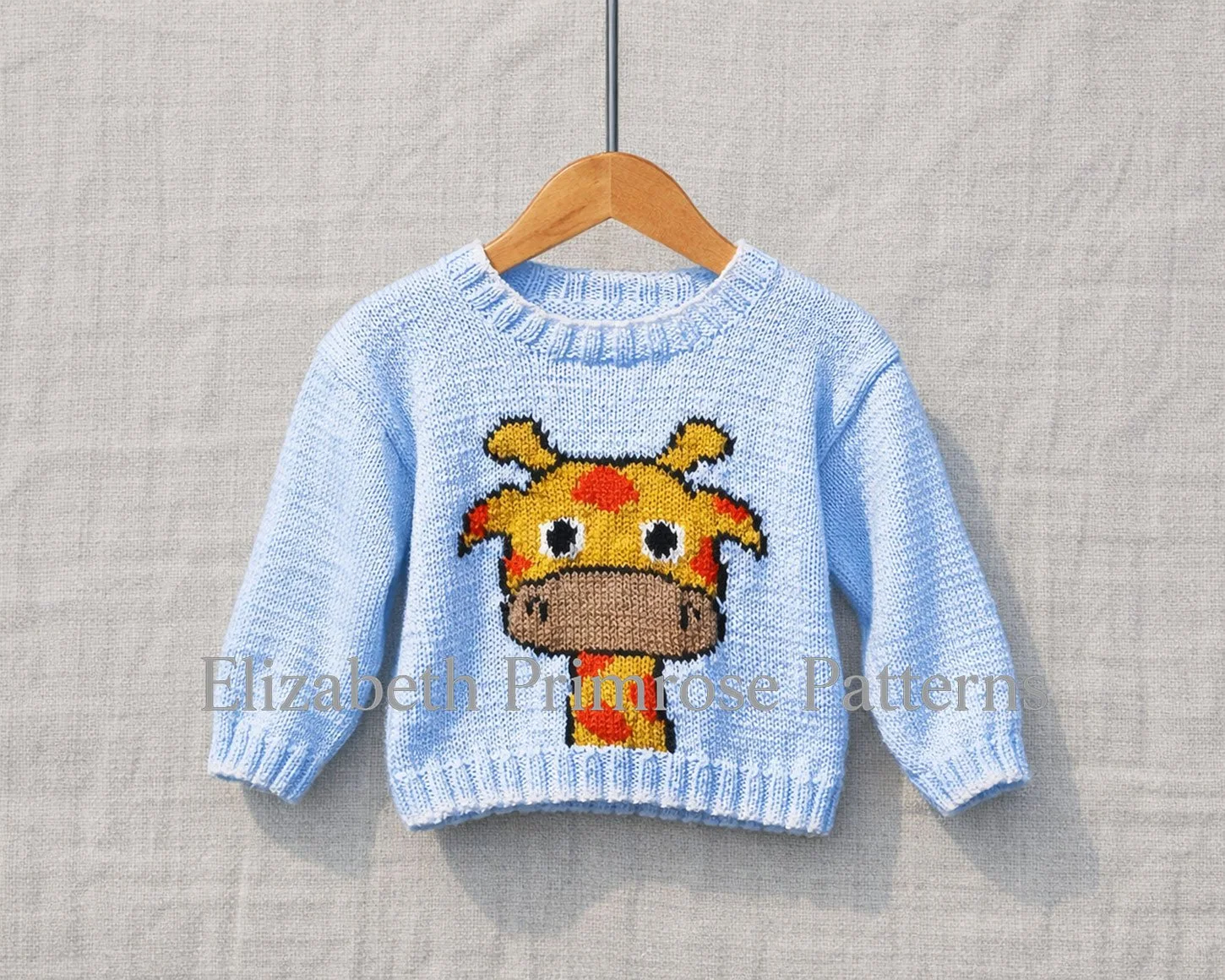 Light blue children’s jumper on a wooden hanger featuring a giraffe motif against a soft, neutral fabric background.