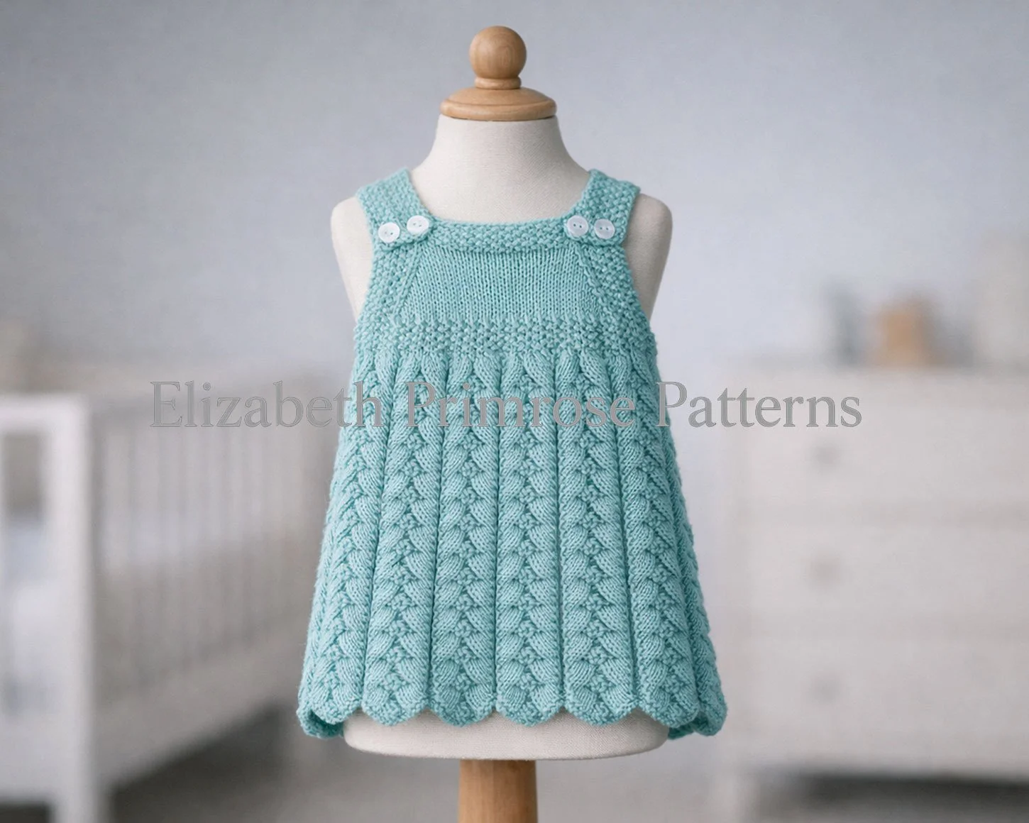Blue herringbone textured baby sundress with buttoned straps displayed on a mannequin in a calm nursery room, knitting pattern.