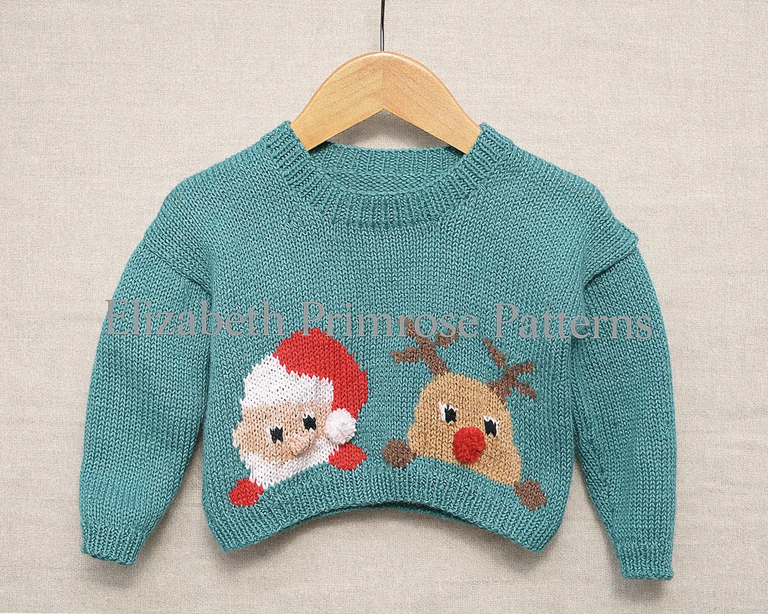 Teal children’s Christmas jumper with Santa and reindeer motifs, hanging on a wooden hanger against a soft neutral background.