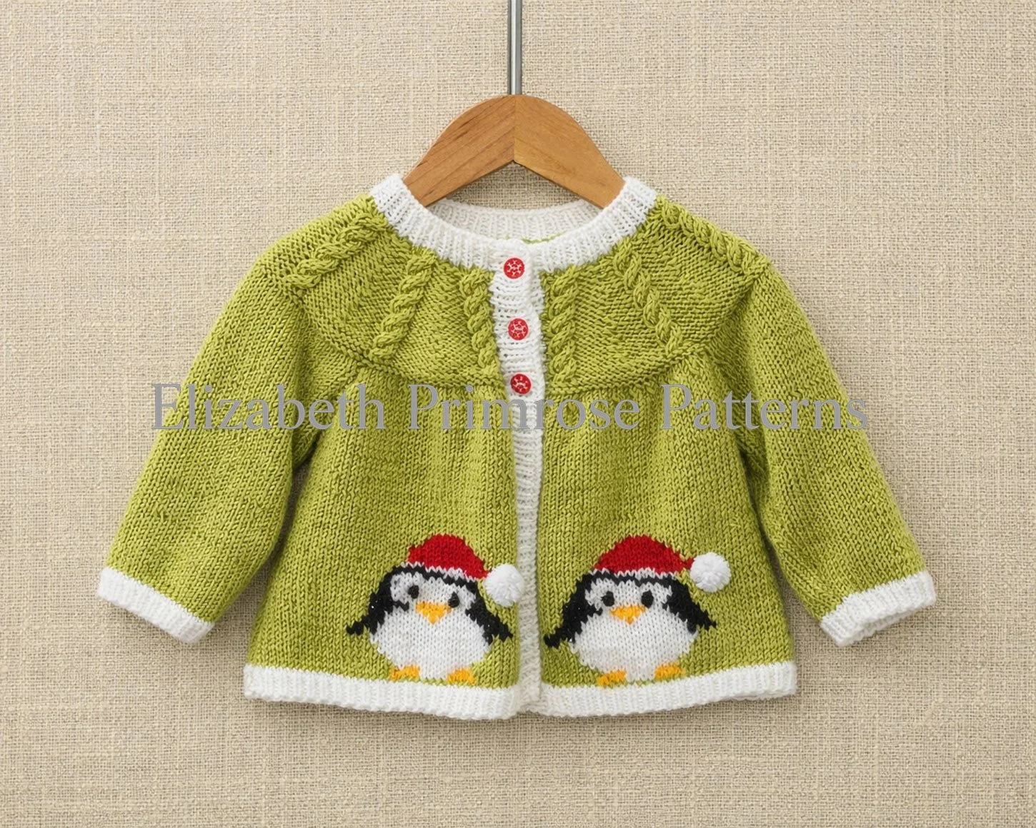Light green baby cardigan with penguin motifs and red buttons, hanging on a wooden hanger against a crisp beige linen background.