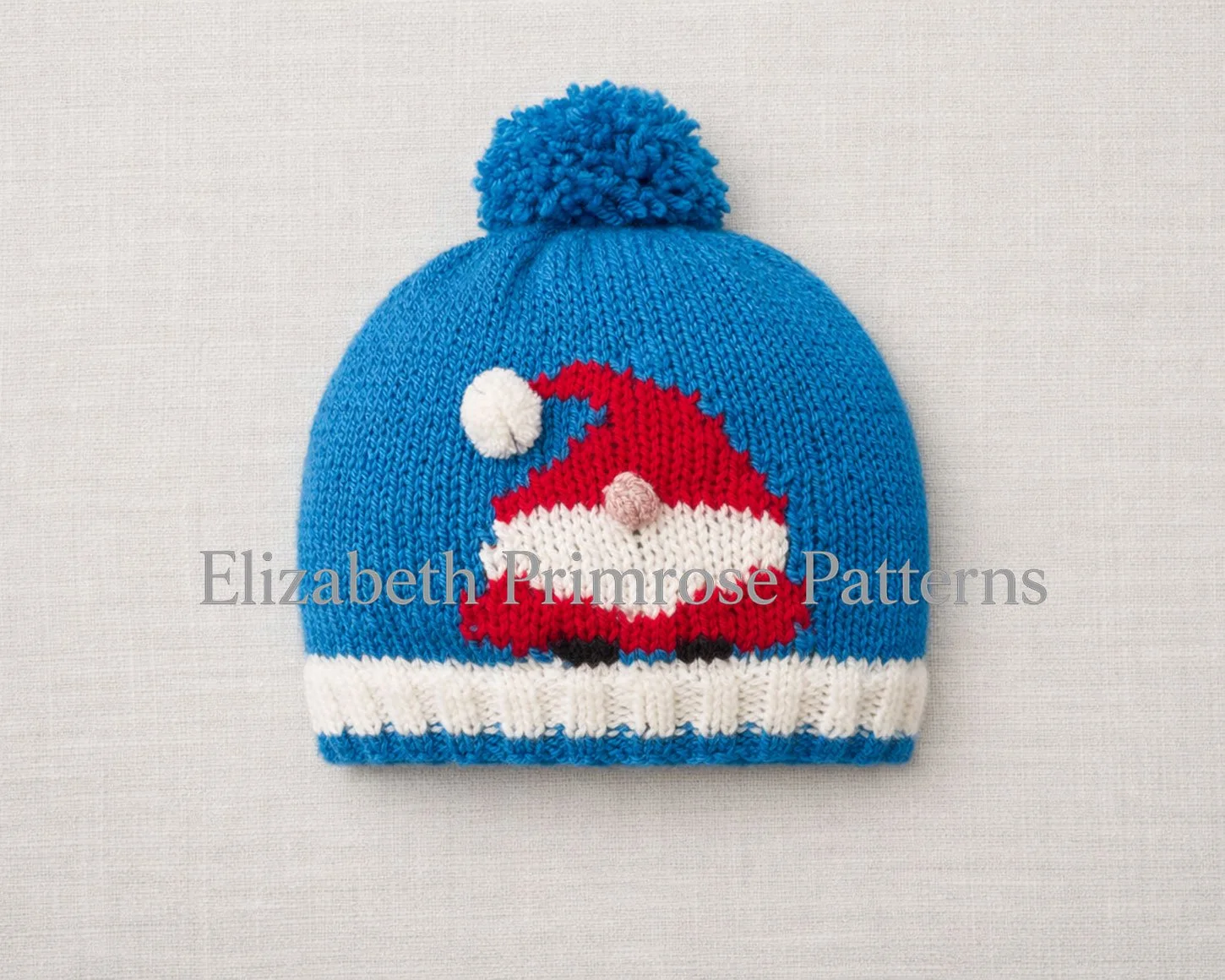 Blue children’s Christmas gnome hat laid flat on a light linen background with pompom and festive motif clearly visible.