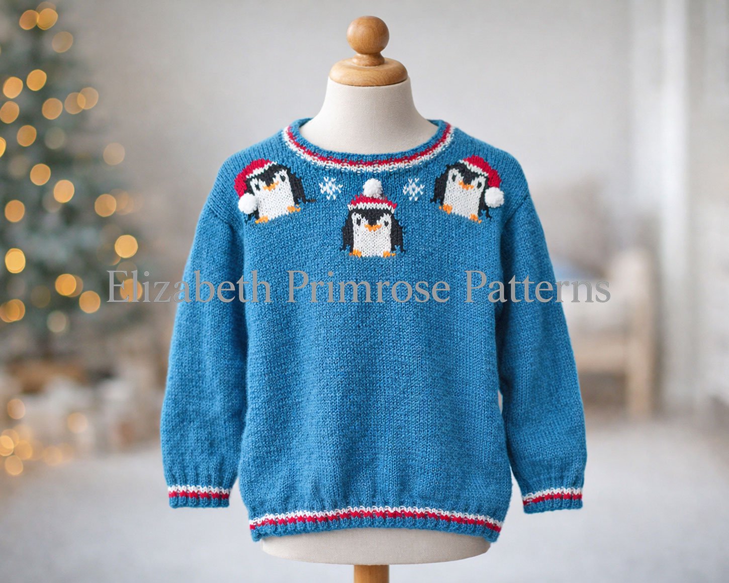 Festive blue knitted jumper featuring three penguins and snowflakes, shown on a child’s mannequin with a softly lit Christmas tree behind.