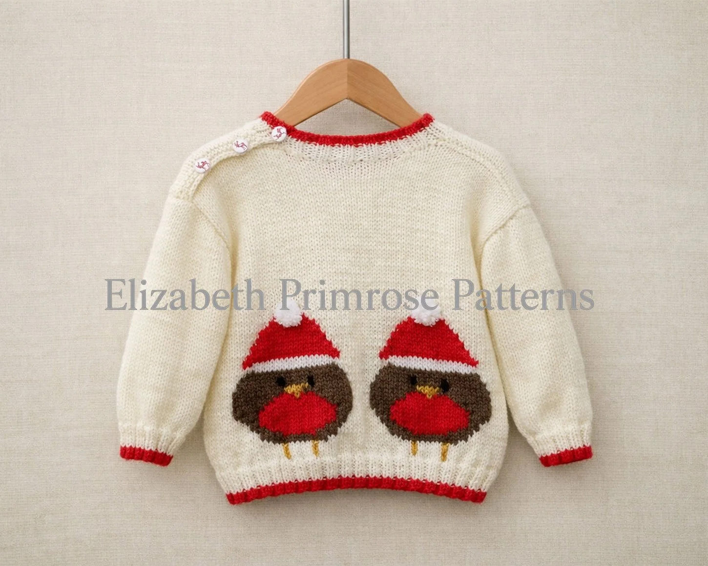 Back of cream children’s knitted jumper with two robin motifs in Santa hats, displayed on a wooden hanger against a soft beige fabric background.