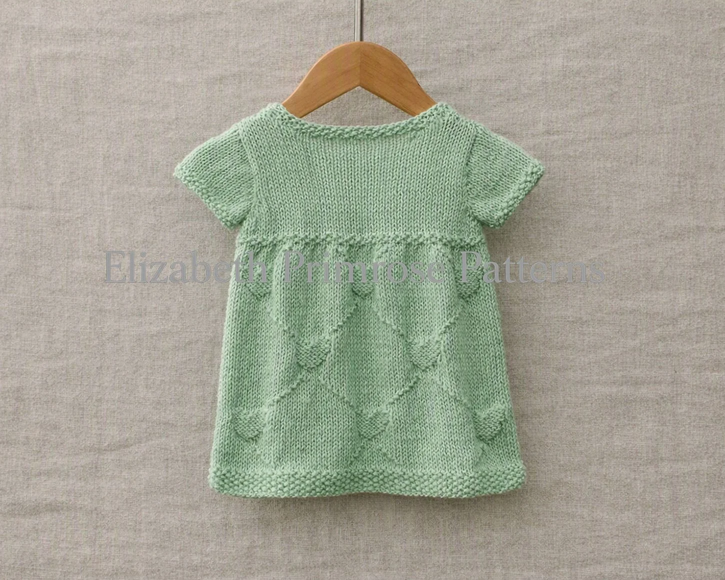 Back view of a mint green short-sleeved hand-knitted child dress with textured diamond pattern.