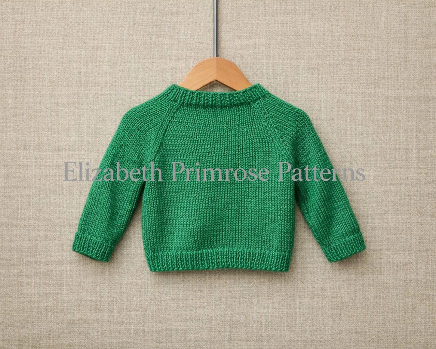 Back view of green children’s jumper with raglan sleeves hanging on a wooden hanger against a soft beige fabric background.