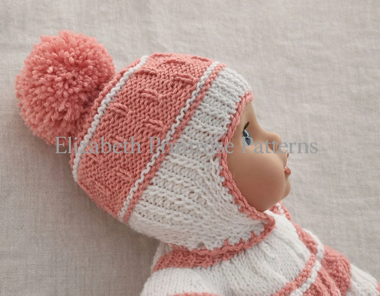 Baby doll in pink and white knitted hat, shown in close side view against a soft beige fabric background with clear stitch texture.