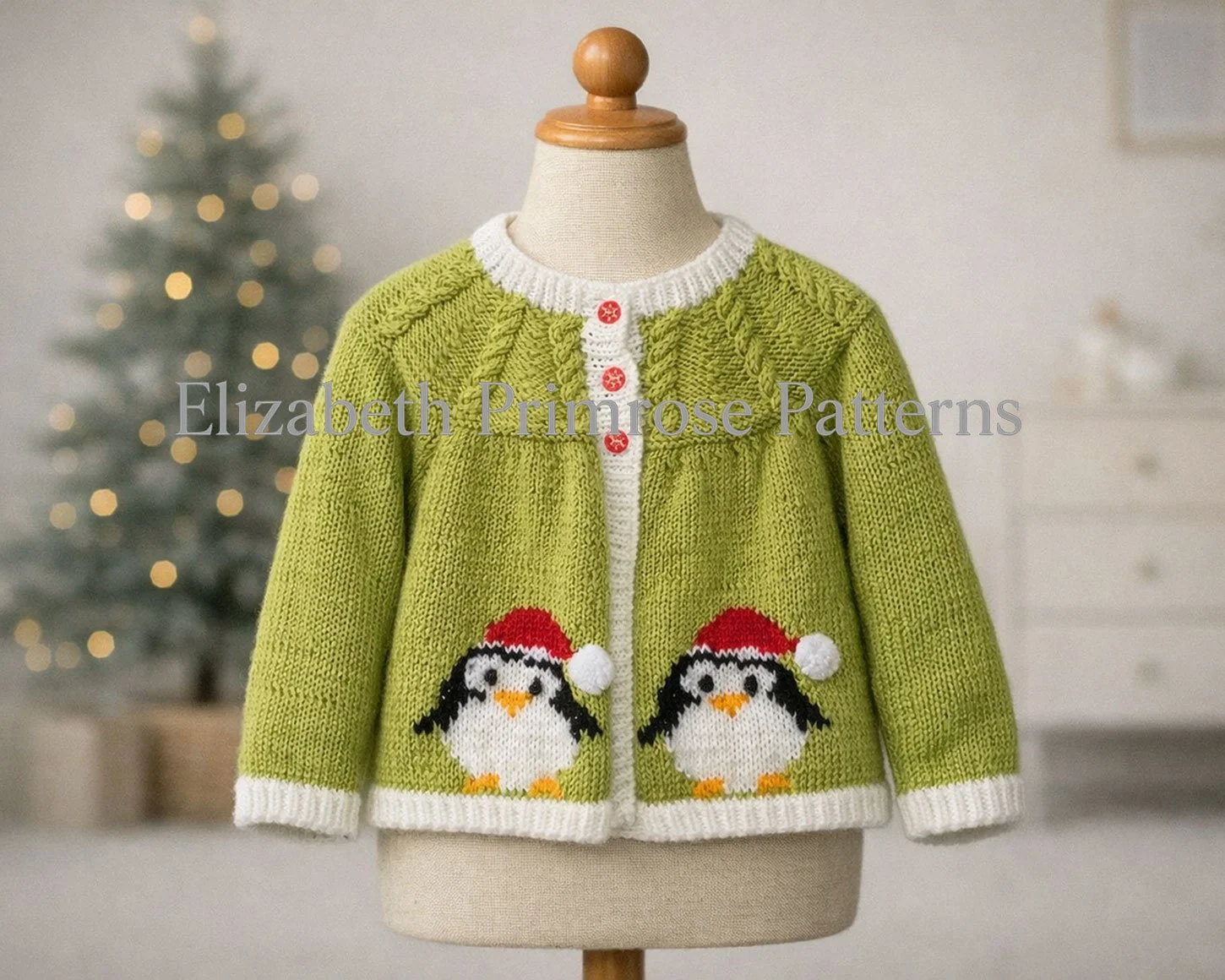 Festive green knitted cardigan with penguin motifs and red buttons displayed on a child’s mannequin, with a softly lit Christmas tree in the background.