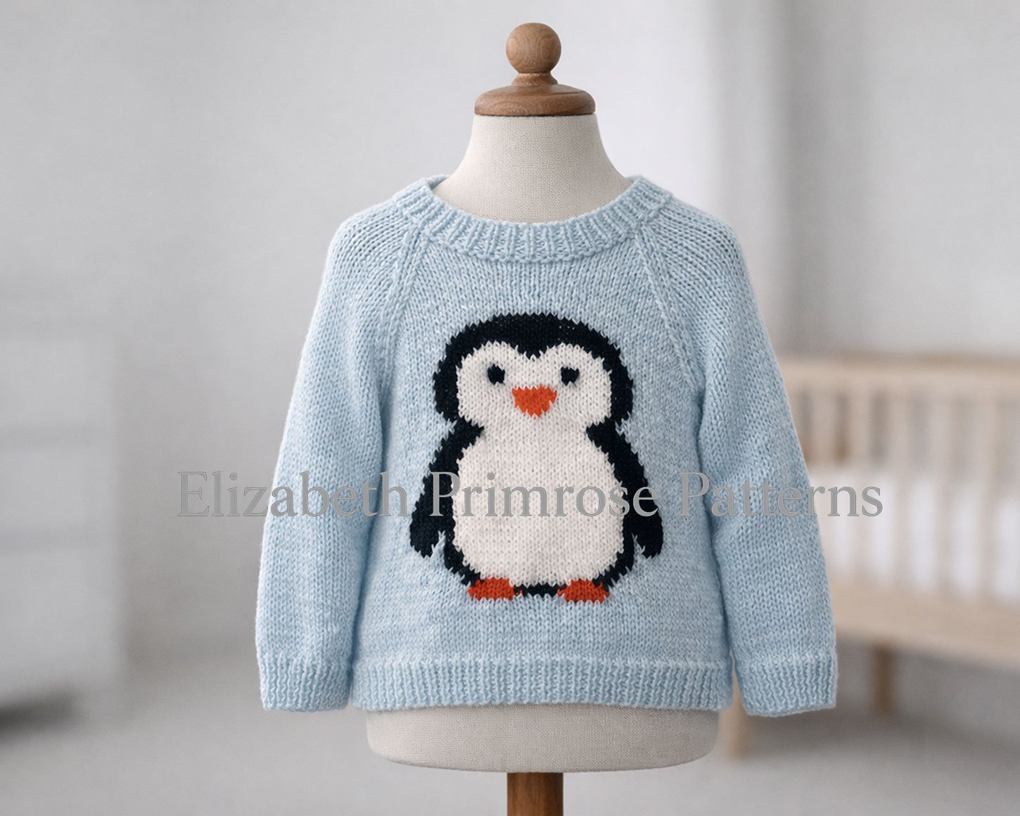 Hand‑knitted light blue sweater featuring a penguin design shown on a child’s mannequin in a calm, neutral room.