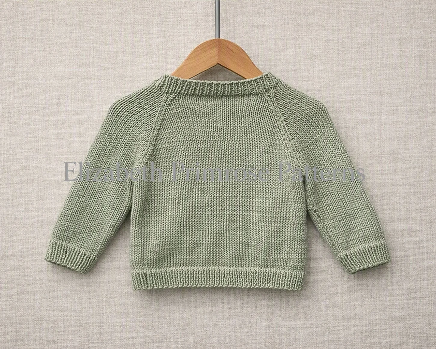 Light green raglan baby sweater displayed on wooden hanger against beige fabric background shown from the back view. Knitting pattern by Elizabeth Primrose Patterns.