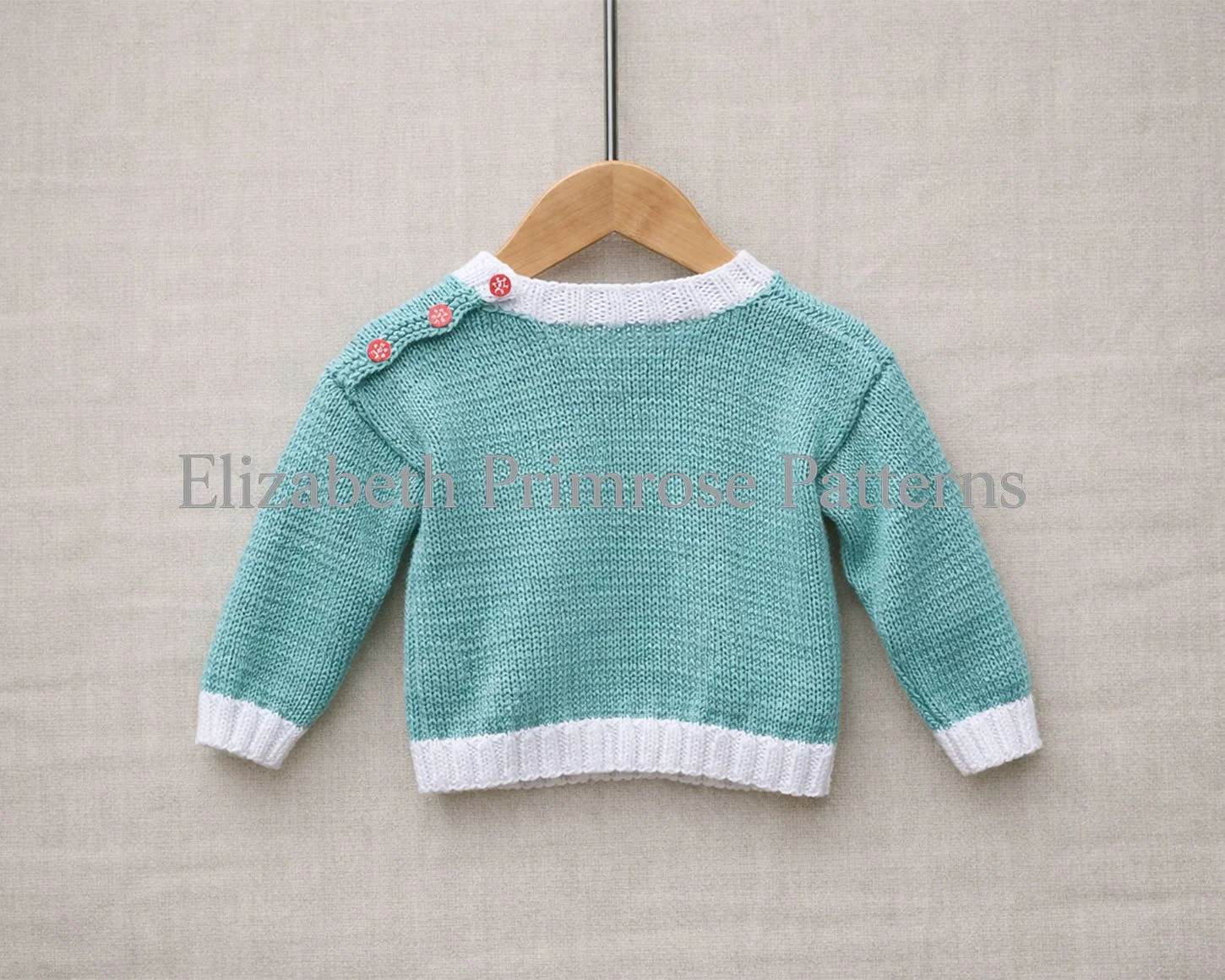 Back view of turquoise children’s jumper with white ribbing and three red shoulder buttons, displayed on a wooden hanger against a neutral fabric background.