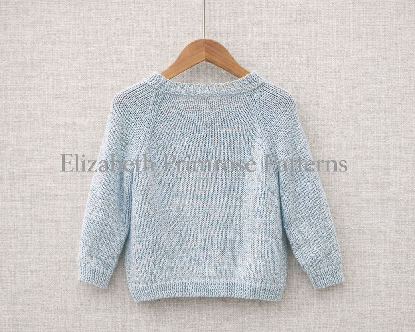 Back view of a light blue knitted sweater displayed on a wooden hanger with a textured beige linen backdrop.