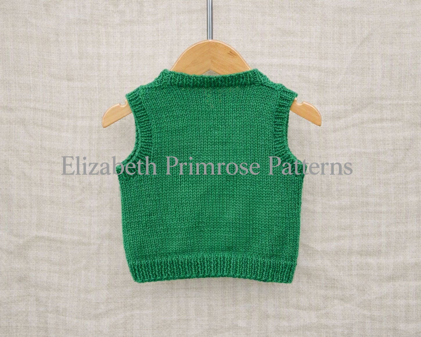 Children’s green knitted tank top on a wooden hanger against a linen backdrop, shown from the back view.