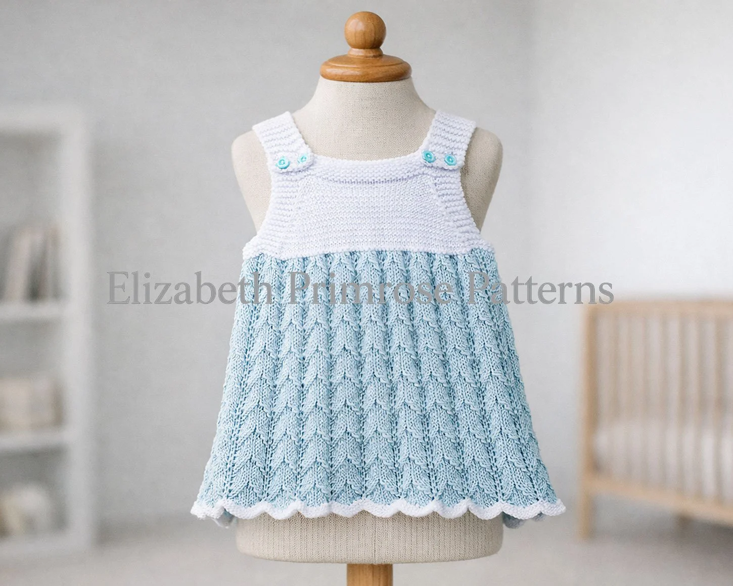 Light blue and white knitted baby dress displayed on a mannequin in a calm nursery setting with soft, diffused lighting.