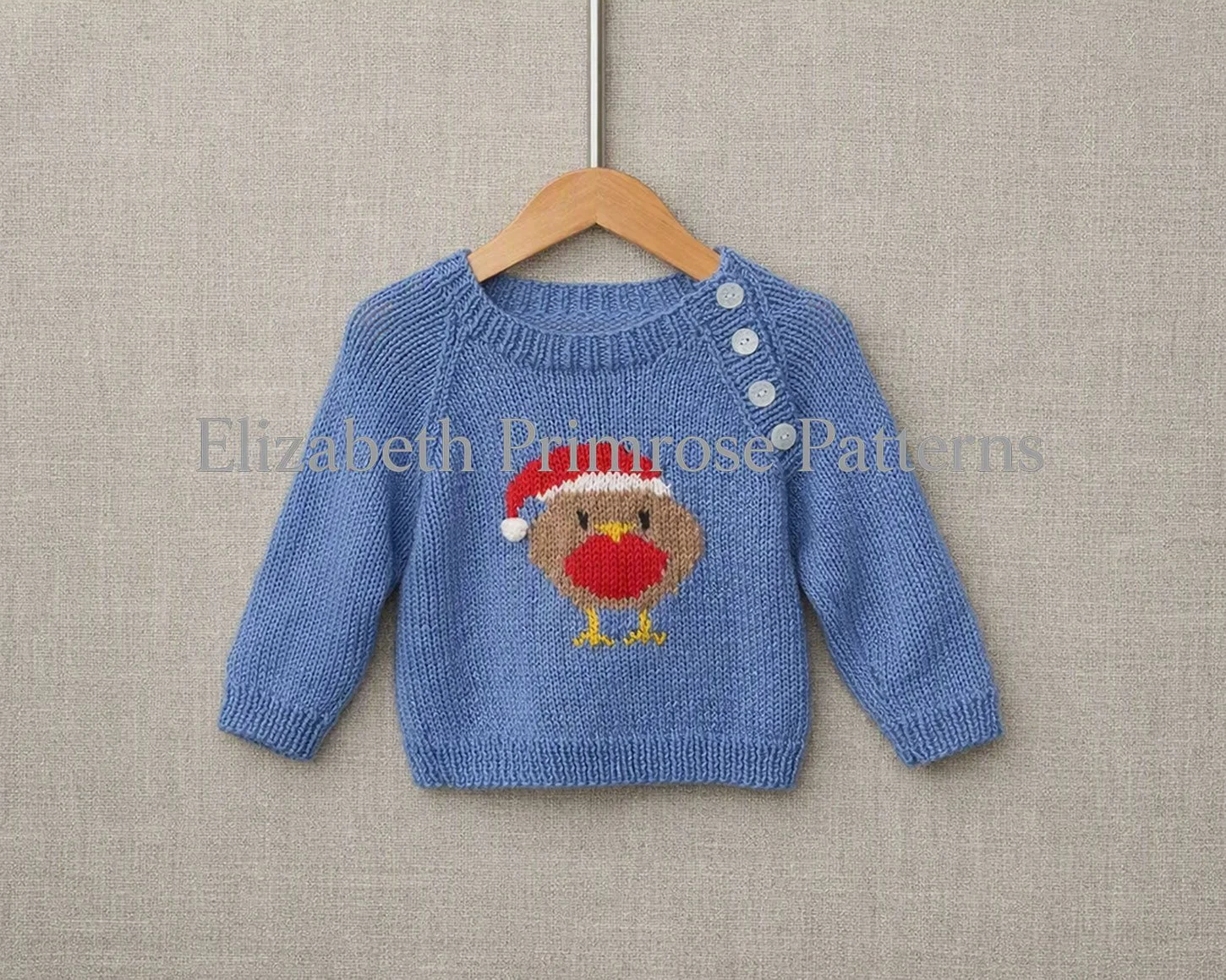 Knitted blue children’s jumper featuring a festive robin motif with raglan sleeves and front buttons, displayed on a hanger against a soft beige backdrop.
