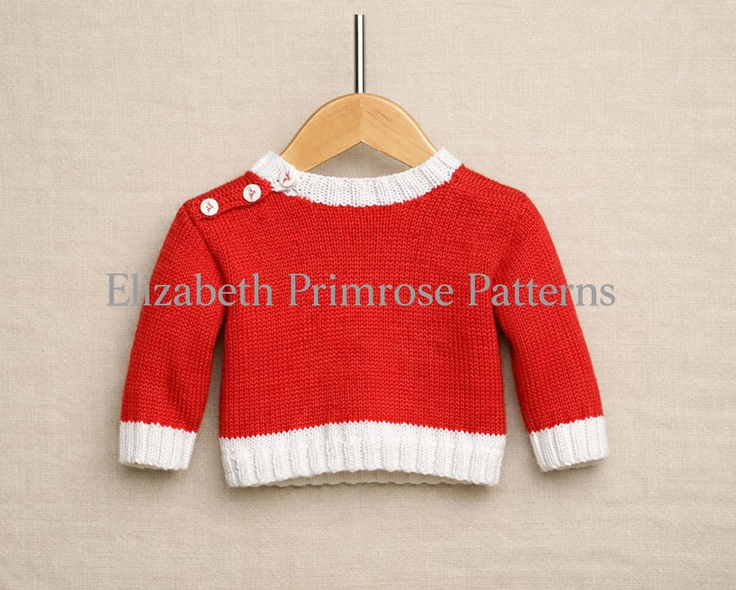 Back of red knitted baby sweater with white ribbed collar, cuffs, and hem, hanging on a wooden hanger with straight metal pole over beige linen.