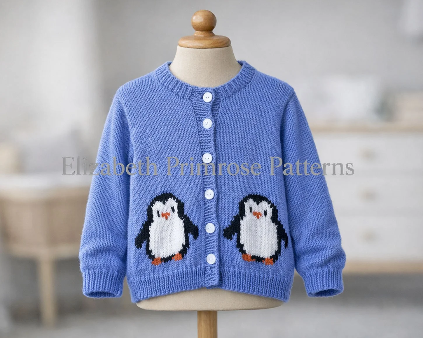 Blue knitted jumper with penguin design, shown on child mannequin with natural sleeve drape and blurred minimalist background.