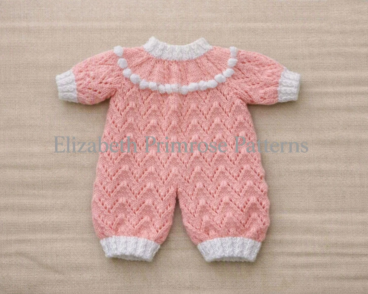 Pink hand-knitted doll romper with an intricate lace chevron pattern, white ribbed cuffs, and a decorative white bobble row along the rounded collar yoke.